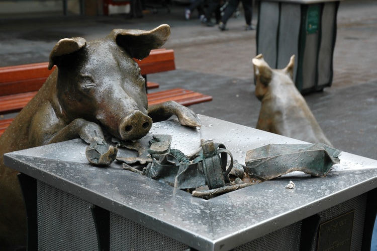 Bronze pig rummages though a rubbish bin