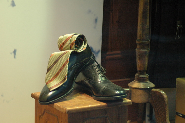 A shop window display with a tie rolled up on top of a pair of shoes