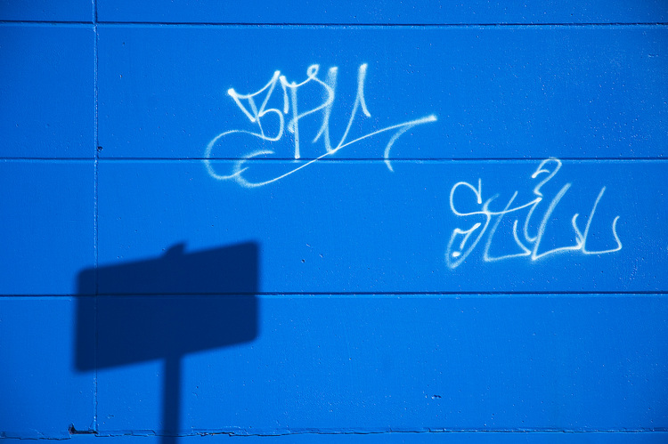 White graffiti on a blue wall, with the shadow of a sign on it