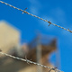 Barbed wire against a blue sky and buildings